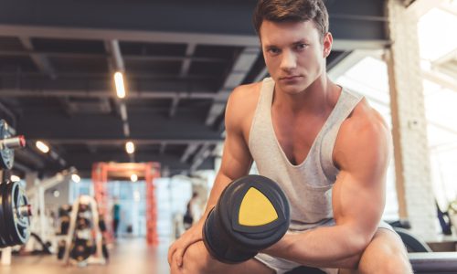 Attractive young muscular man is working out with dumbbells in gym