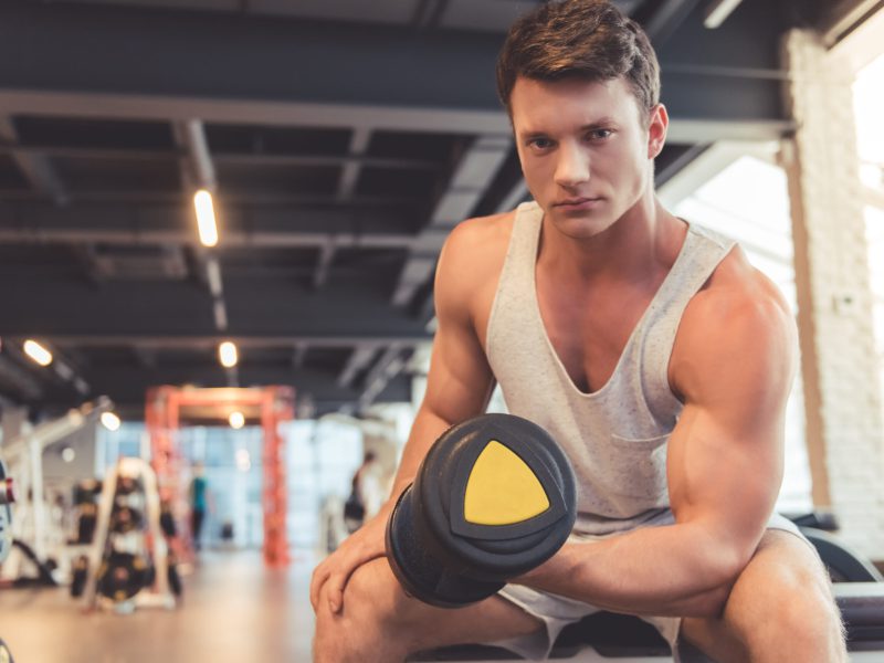 Attractive young muscular man is working out with dumbbells in gym